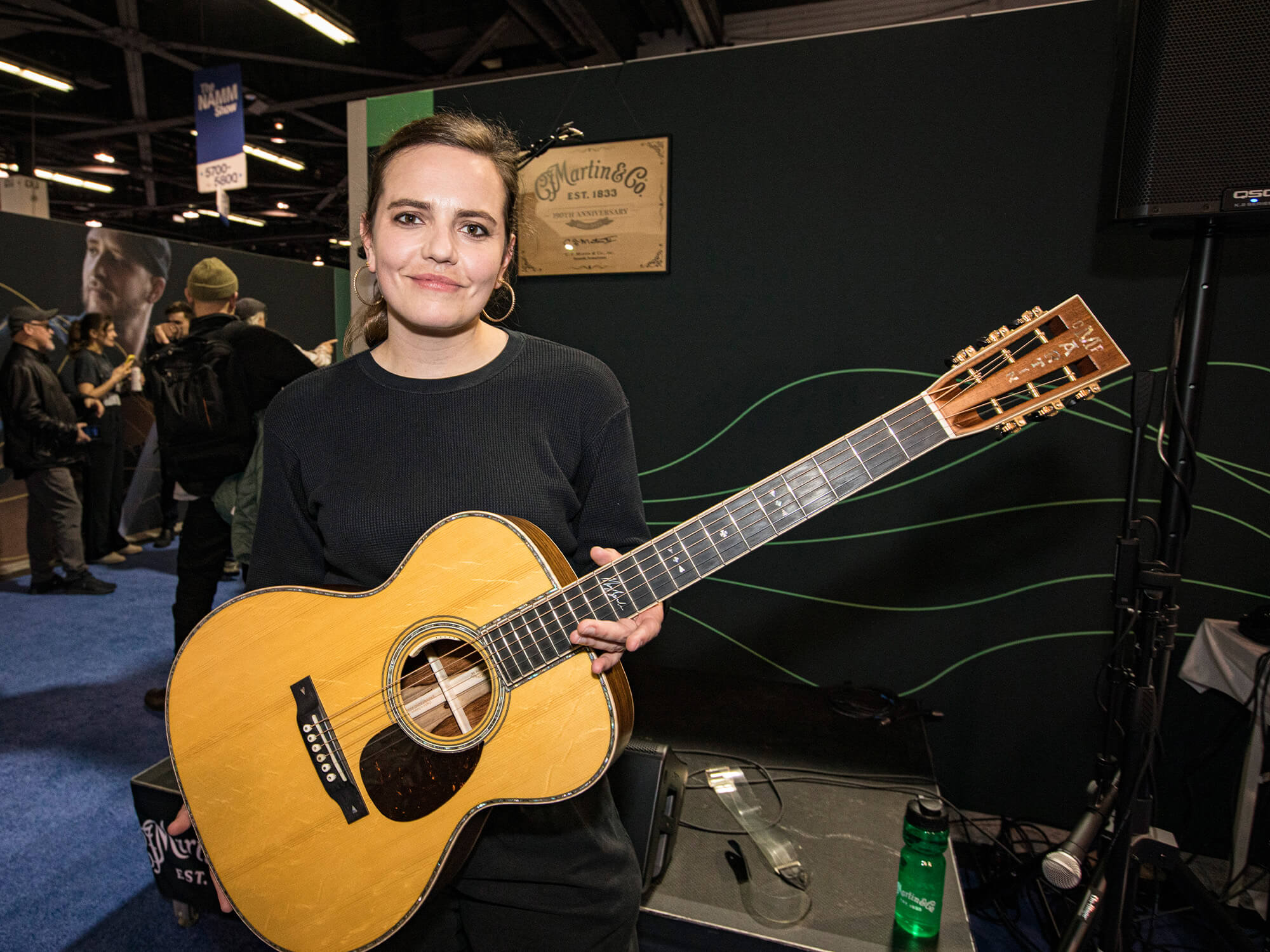 Mary Spender at The NAMM Show 2024. She is holding a Martin acoustic and is smiling at the camera.